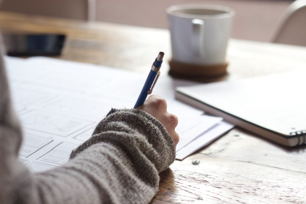 person-writing-on-brown-wooden-table-near-white-ceramic-mug-s9cc2skysjm Designer sketching Wireframes